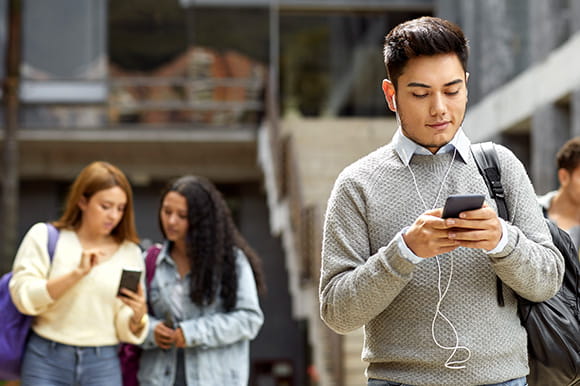 Male student texting from cell in campus. Young man listening to music at university. He is using smart phone.